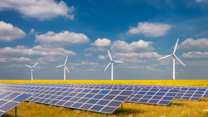 Windräder und Solarkraftwerk auf Feld mit gelben Pflanzen vor blauem Himmel