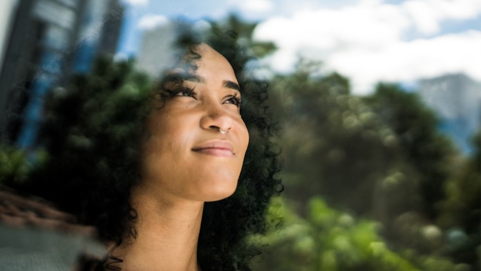 Junge Frau blickt auf dem Fenster in die Ferne