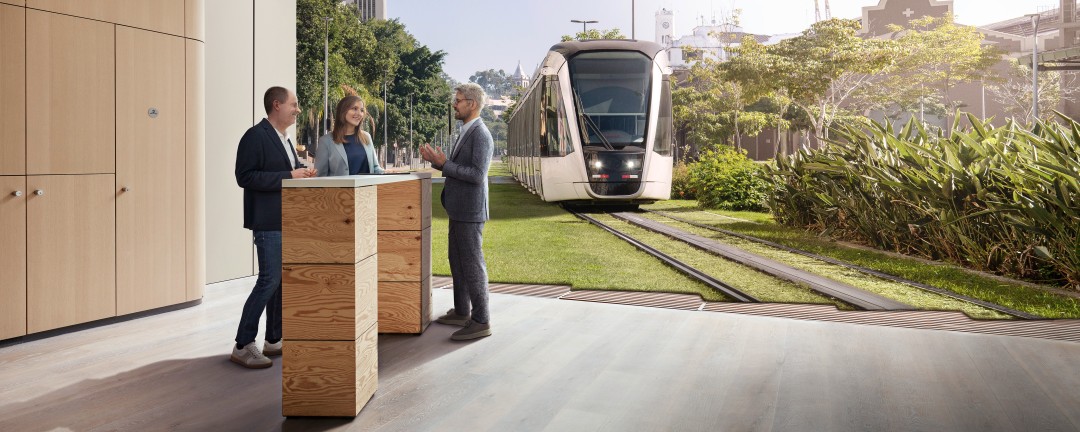 Drei Personen unterhalten sich in einer Arbeitssituation an einem Stehtisch. Im Hintergrund ist ein Bild einer Bahn in grüner Umgebung eingeblendet.