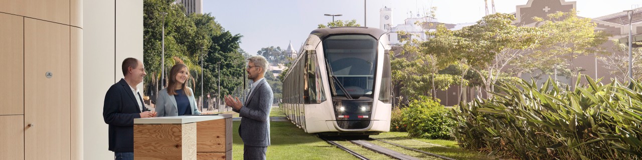 Three people are talking in a work situation at a high table. In the background, an image of a train in a green environment.