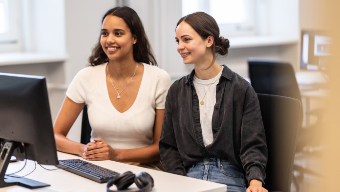 Two young women are sitting in front of a computer