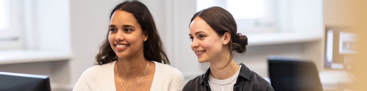 Two young women are sitting in front of a computer