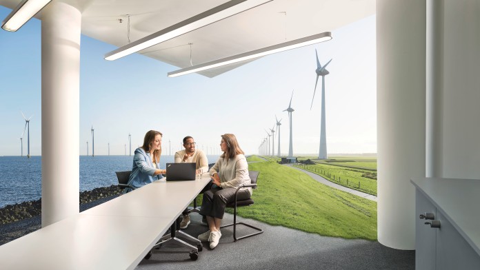 Three people sit in front of a laptop at a long table. Onshore and offshore wind turbines are shown in the background