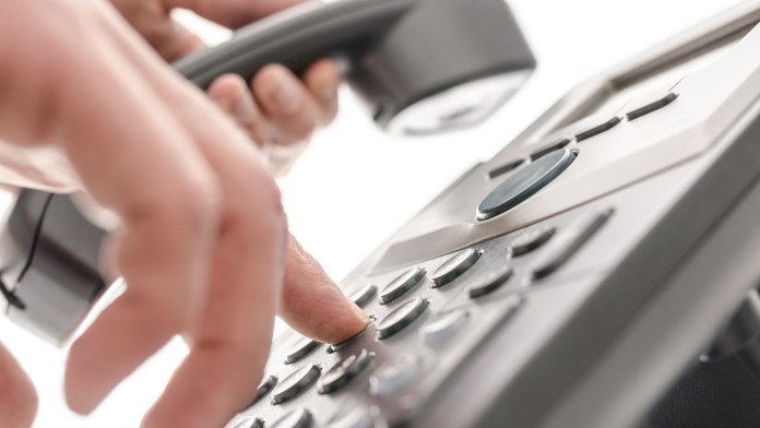 A hand is dialling on an office telephone