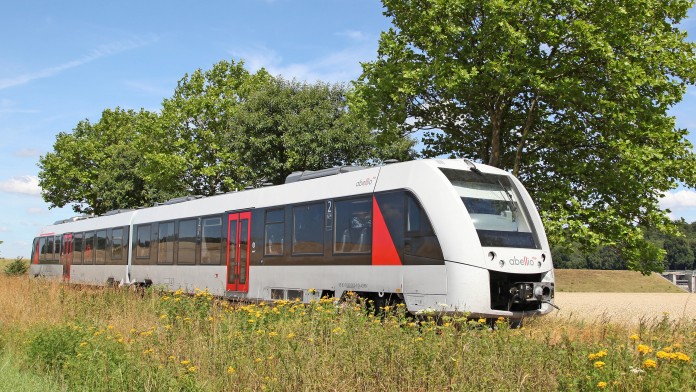 Personenzug fährt vorbei an Wiesen und Bäumen vor blauem Himmel