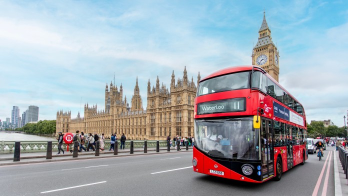 Roter Doppeldeckerbus fährt auf einer Brücke vor Londoner House of Parliament