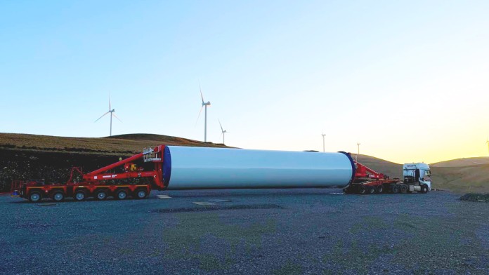 Teil eines Windrads wird vopn LKW transportiert; im Hintergrund sind Windräder