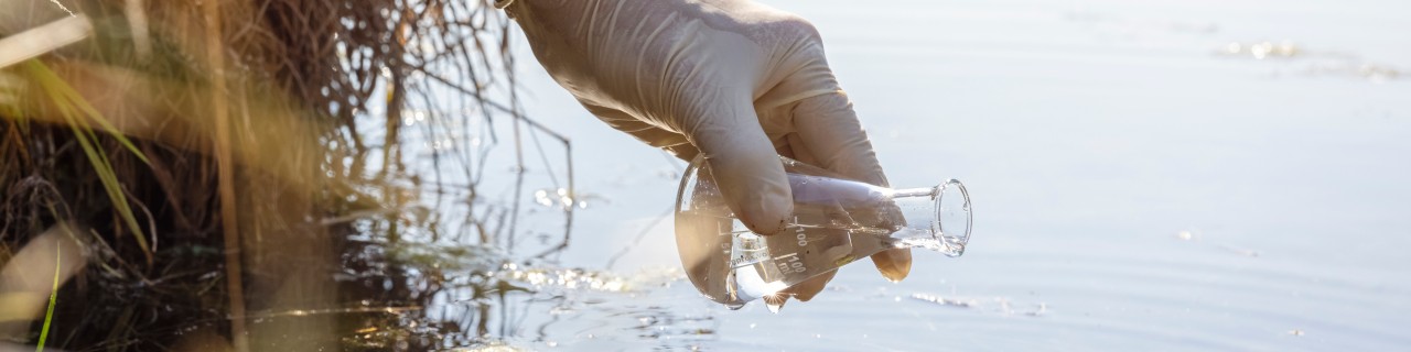 A hand holding a test tube over a body of water