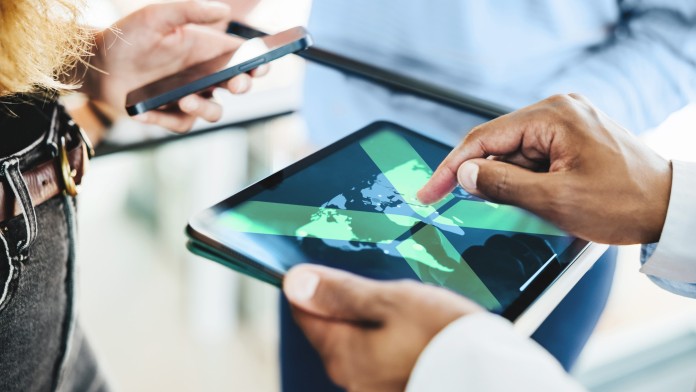 Hände bedienen ein Tablet, auf dem eine digitle Weltkarte zu sehen ist. Die Bildthemen sind Datenanalyse, globale Vernetzung und digitale Transformation.